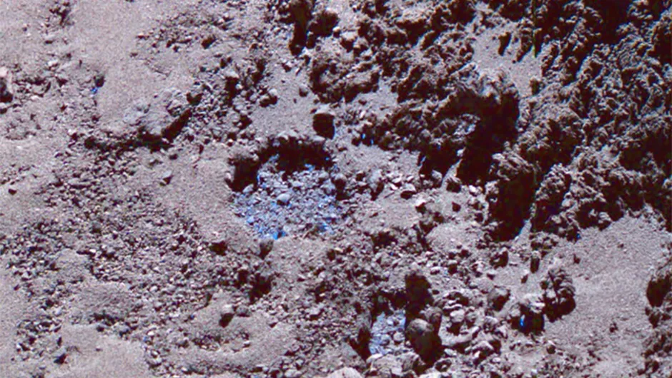 An image of the surface of Comet 67_/Churyumov-Gerasimenko. On 3 July 2016 a dusty plume erupted from the ice-filled depression close to the large boulder near the bottom of the picture. This image is a false colour composite, and pale blue patches highlight the presence and location of water ice.Credit: ESA/Rosetta/MPS for OSIRIS Team MPS/UPD/LAM/IAA/SSO/INTA/UPM/DASP/IDA