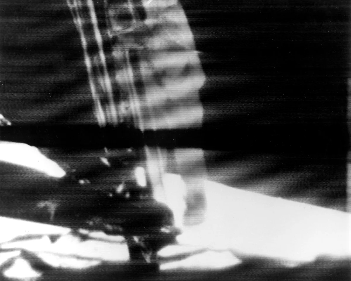 A reproduction of the television image that was broadcast to the world on 20 July. Neil Armstrong is seen descending the Lunar Module ladder, ready to set foot on the surface of the Moon. The black bar across the centre of the image is caused by an anomaly in the TV Ground Data System at Goldstone Tracking Station. Credit: NASA