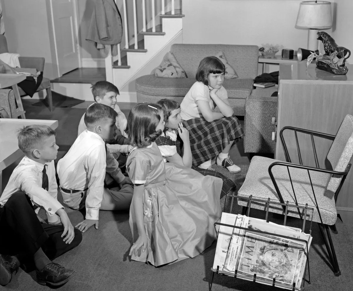 UNITED STATES - Circa 1960s: Side View Of 3 Pairs Of Girls & Boys Dressed Up Gathered Around Television Set.