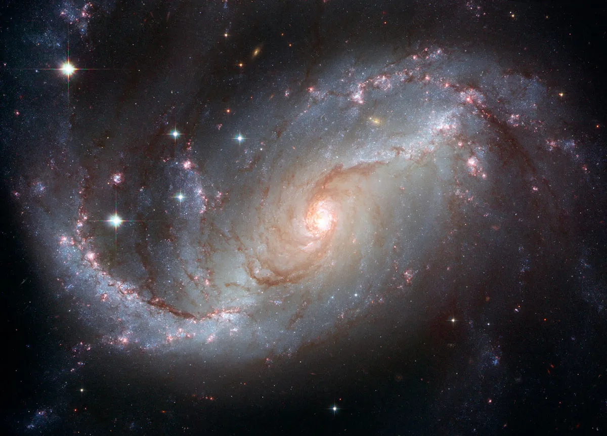 A Hubble Space Telescope image of spiral galaxy NGC 1672. Red and blue spiral arms draw the eye inwards towards the bright centre. Credit: NASA, ESA