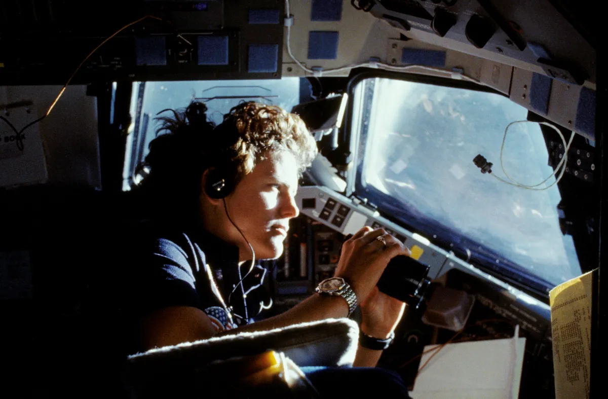 Kathryn Sullivan, the first American woman to spacewalk, uses binoculars to get a better view of Earth from the Space Shuttle cabin window, 6 October 1984. Credit: NASA