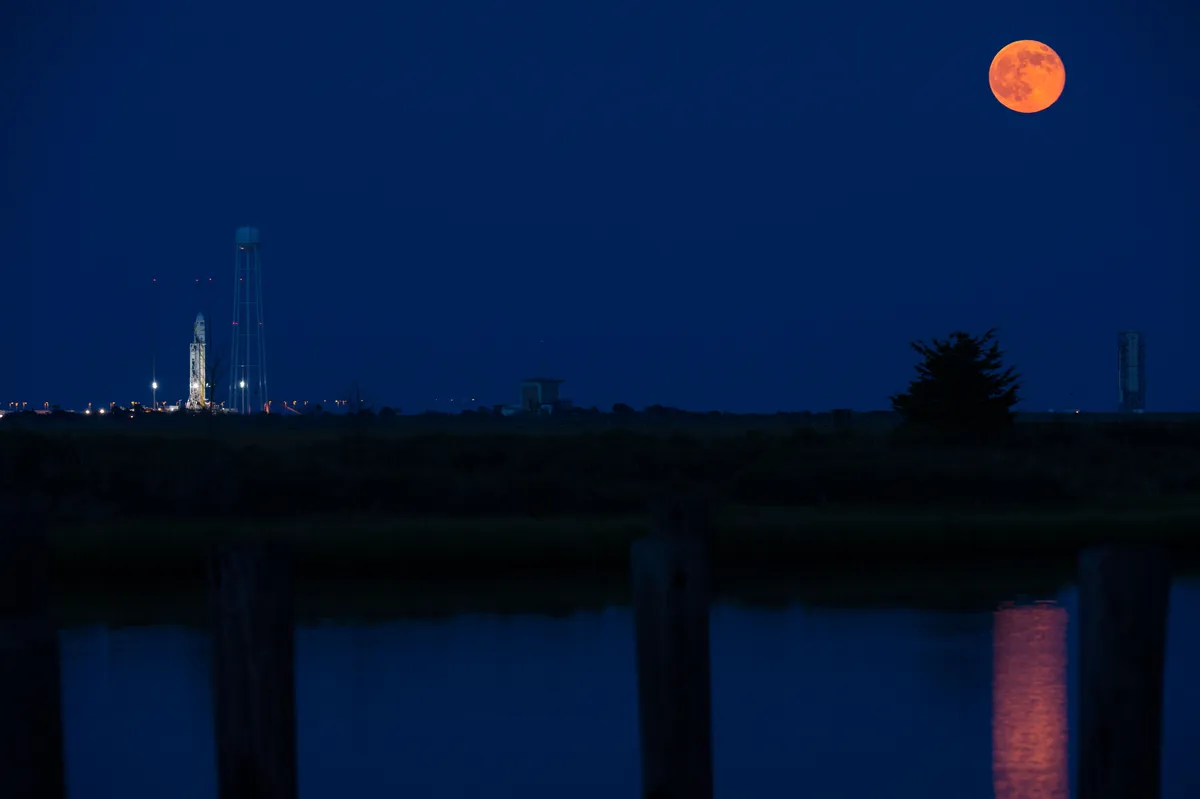 The full Moon seen to the right of the Orbital Sciences Corporation Antares rocket, with the Cygnus spacecraft onboard, Saturday, July 12, 2014, launch Pad-0A, NASA's Wallops Flight Facility in Virginia.