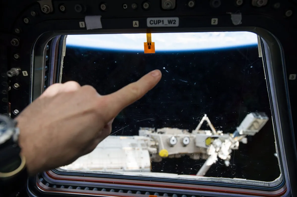 An astronaut points to a micro meteor orbital debris strike on one of the space station's windows. Credit: NASA