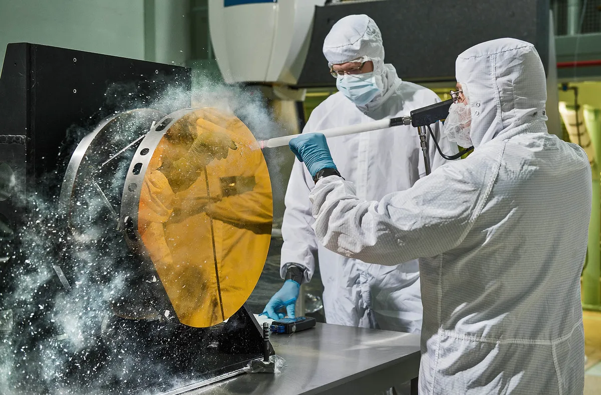 Engineers clean a test telescope mirror for the James Webb Space Telescope by blasting carbon dioxide snow at it. This technique helps to avoid scratching the delicate surface. Credit: NASA/Chris Gunn