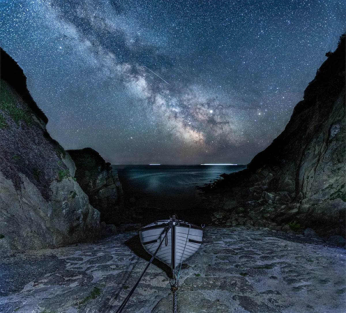 Milky Way and Meteor at Porthgwarra Jennifer Rogers (UK). Category: People & Space. Equipment: Canon 5D Mk IV camera, ISO 1250 Sky: 17mm f/4 lens, boat and foreround: 17mm f/8 lens, cliffs and meteor: 17 mm f/4 lens.