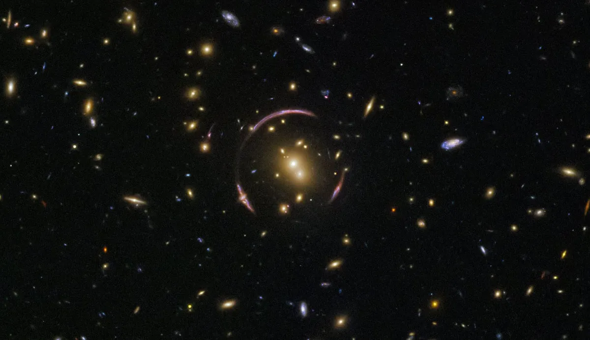 The circular shape surrounding the bright galaxy cluster in the centre of the image is known as an Einstein ring. It's caused by light from distant galaxies being warped by the mass of the cluster in front of it. The idea that mass can warp spacetime was predicted by Einstein in his general theory of relativity. Credit: ESA/Hubble & NASA. Acknowledgement: Judy Schmidt