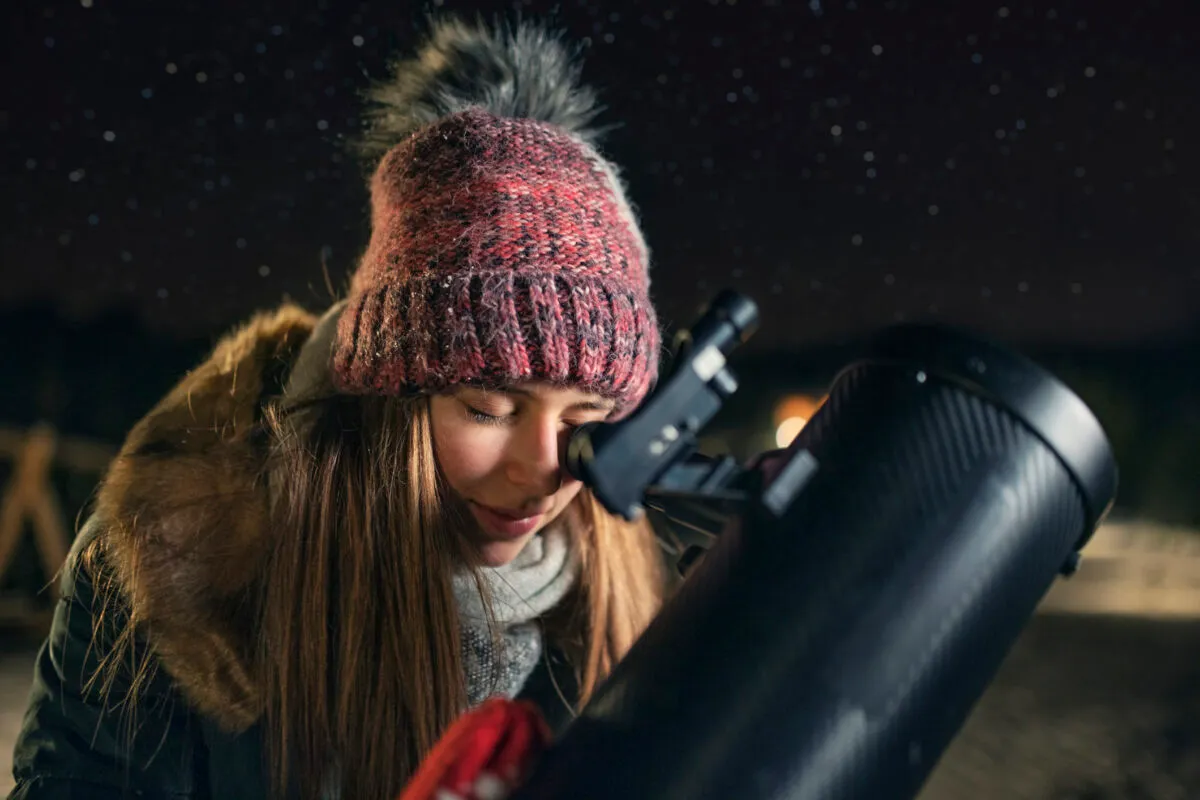 Teenage girl observing the winter night sky with telescope