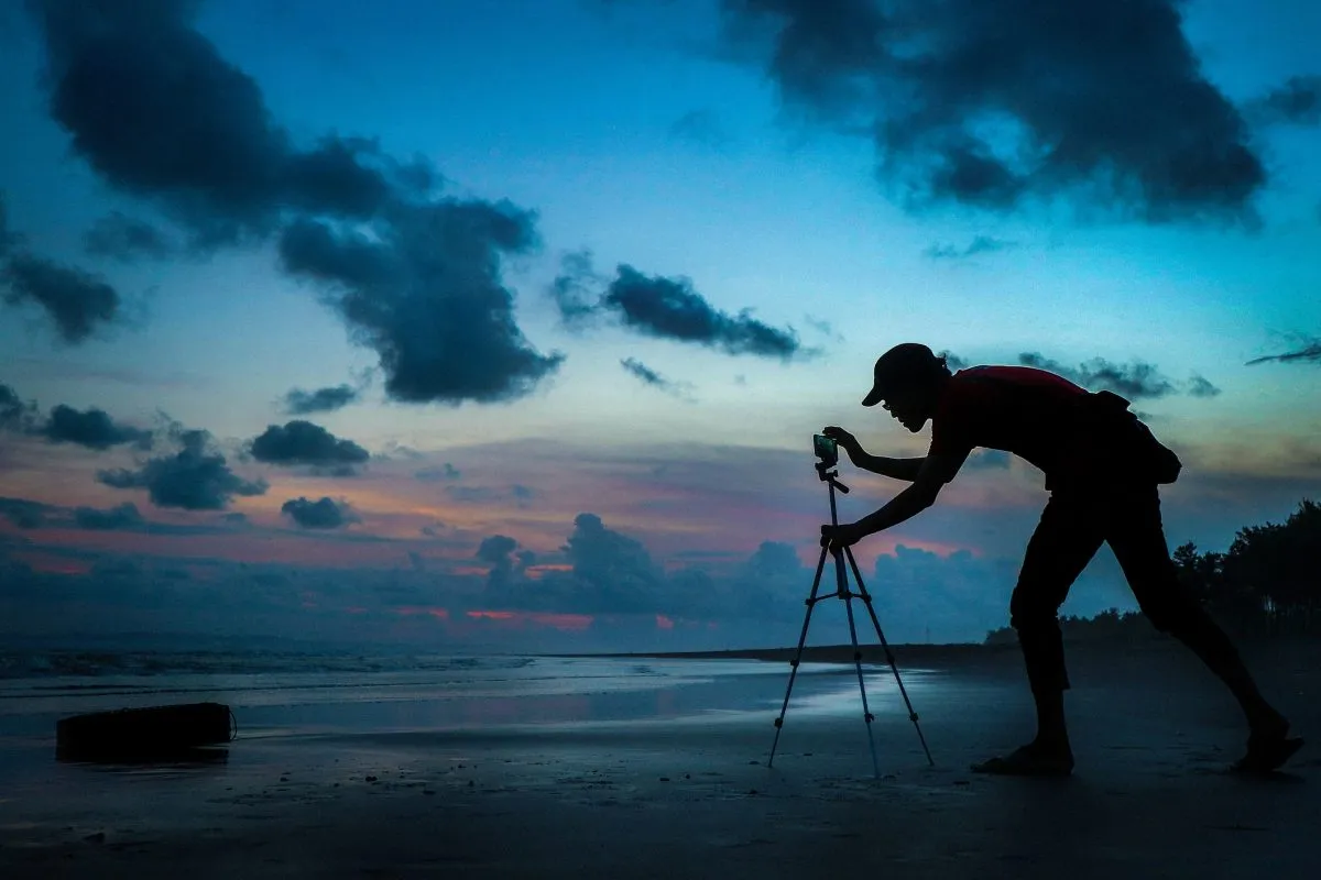 Silhouette of a man adjusting a smartphone on a tripod at dusk