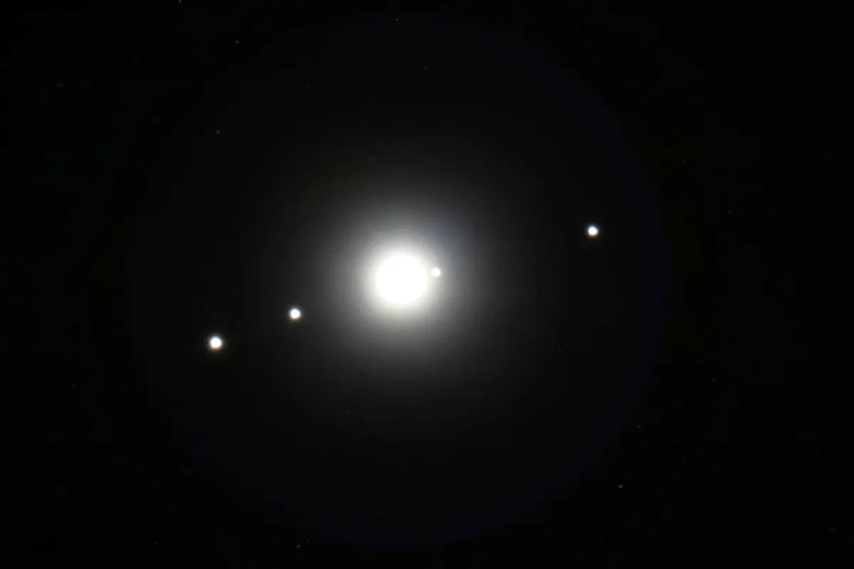 Las cuatro brillantes lunas galileanas de Júpiter aparecen en una sola línea, titilando como estrellas cerca del planeta