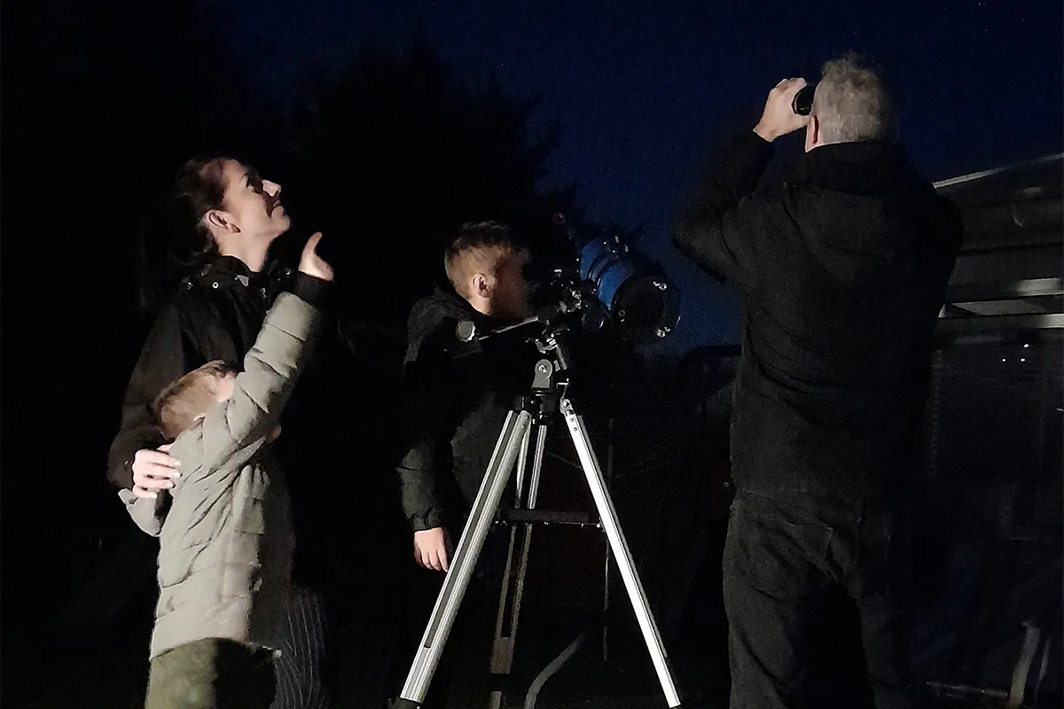 A family with young children observing the night sky through a telescope