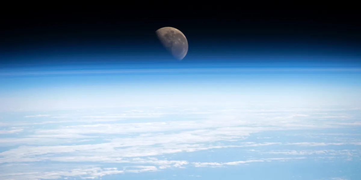 The Earth in the foregound with the Moon appearing above the diffuse atmosphere.
