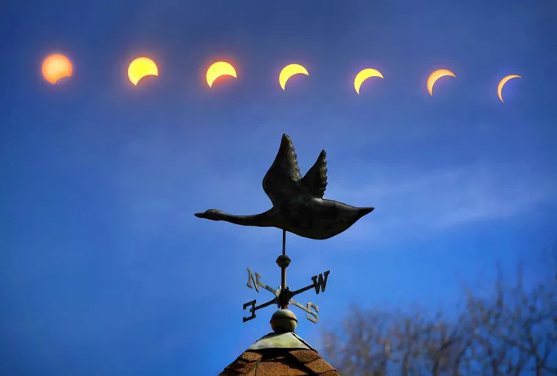 An in-camera multiple exposure sequence of an hour showing seven stages of the solar eclipse through different amounts of totality as seen over a snow goose weathervane on a cupola. Photo by John Tlumacki/The Boston Globe via Getty Images