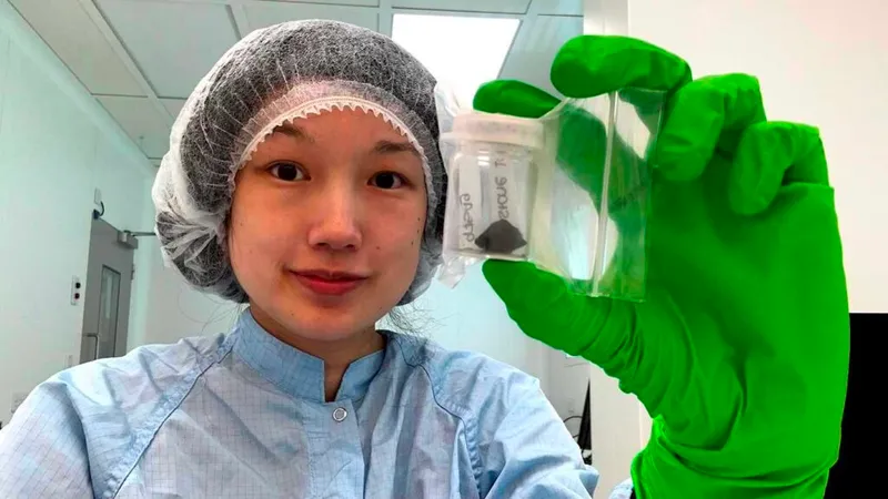 Queenie Chan in clean room gear holding a piece of Winchcombe Meteorite for analysis. It is black, the size of a walnut and sealed inside a jar.