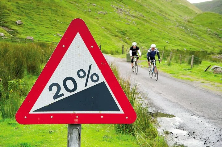 Cyclists ride past a 20% gradient sign on a cycling route in the Scottish Borders