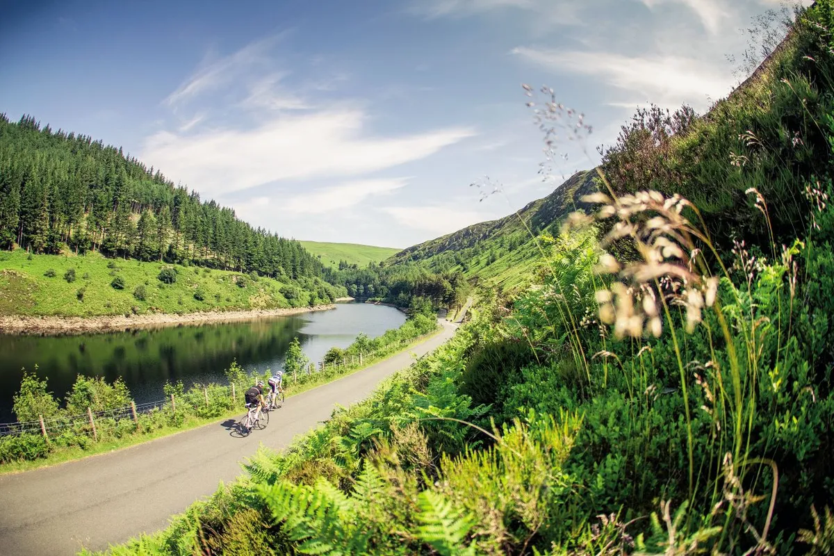 Two cyclists ride past a reservoir in the Elan Valley, Wales