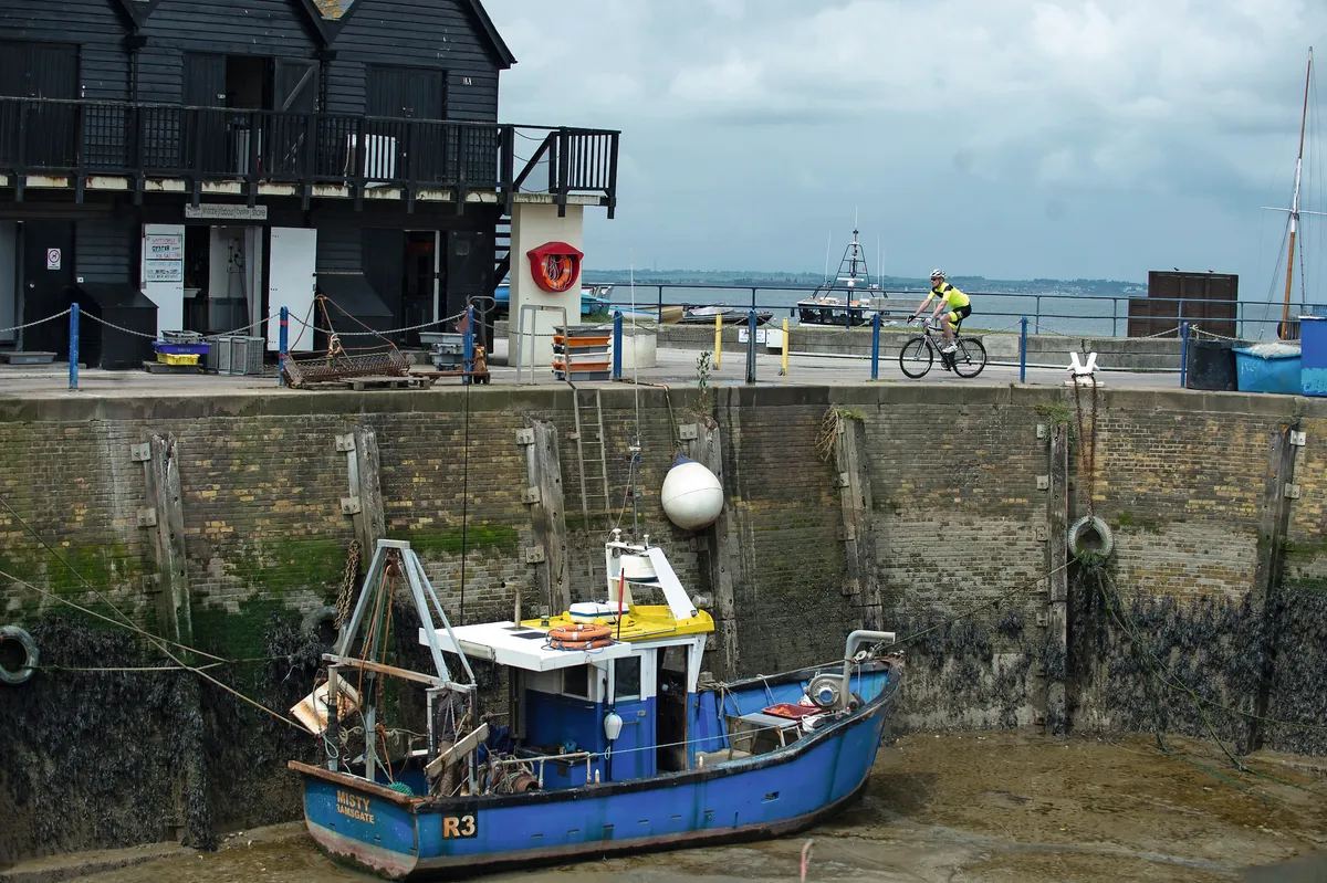 Cyclist riding on a harbour wall above a blue fishing boat