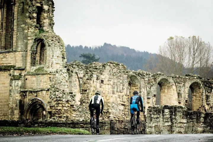 Two cyclists riding past the ruins of an abbey in the North Yorkshire Moors