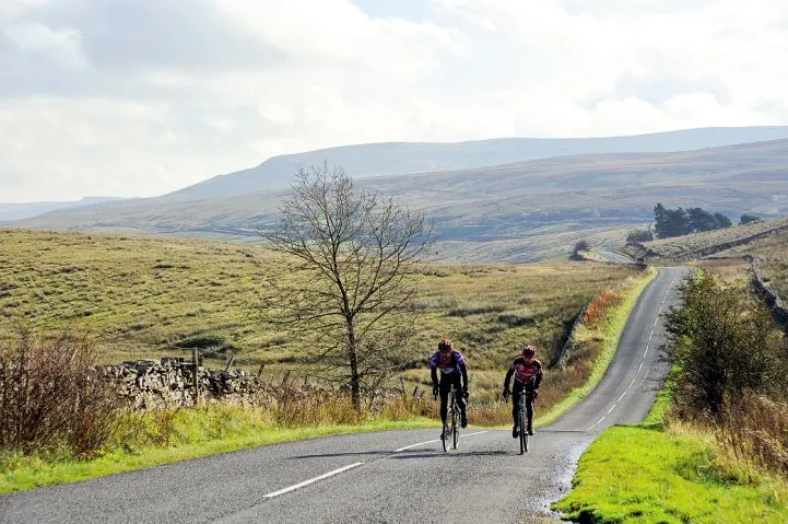Two cyclists riding on an empty, straight road in the Yorkshire Dales