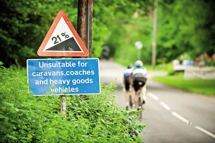 Two cyclists ride past a 21% gradient sign in the Surrey Hills