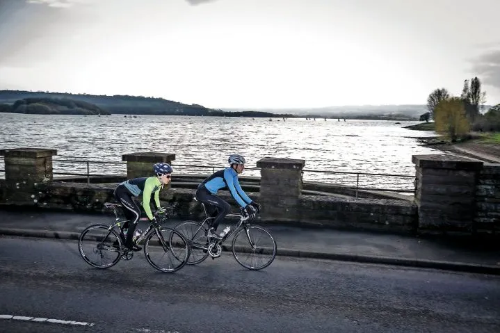 Two cyclists ride past water in Somerset