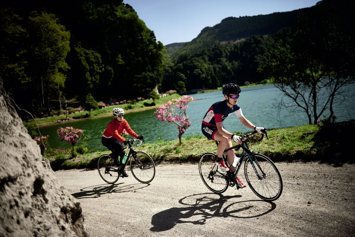Two cyclists riding in the Azores with a lakeland background
