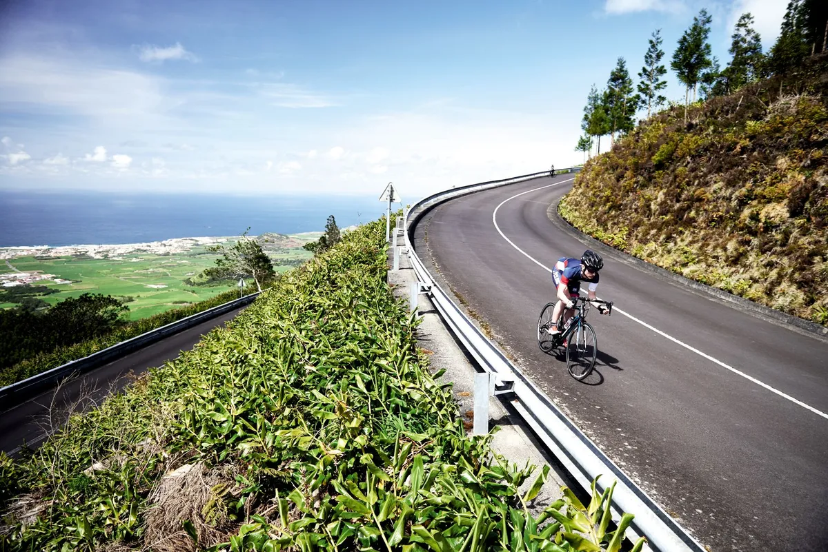 A cyclist swoops downhill on a smooth road in the Azores