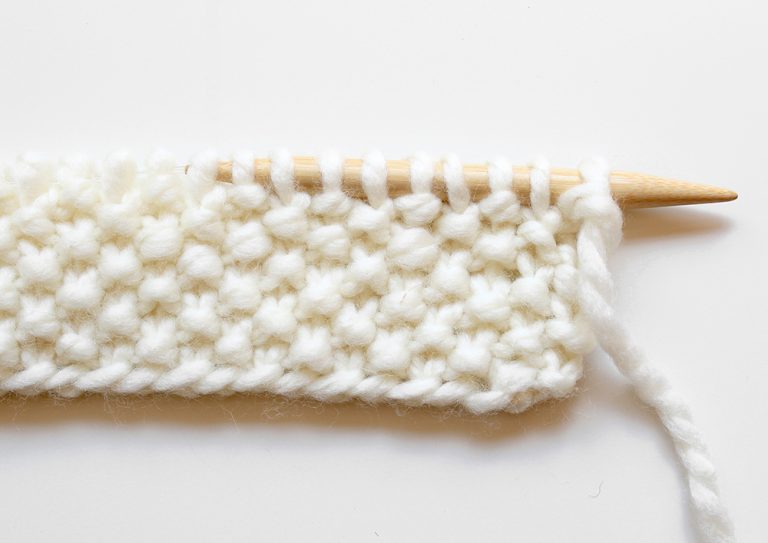 The moss stitch border of the how to knit a baby blanket tutorial is shown on a needle