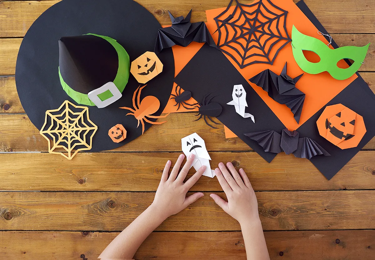 Paper toys of origami for Halloween on wooden background. Hands of kids. Lesson of origami. Preparation for a holiday.