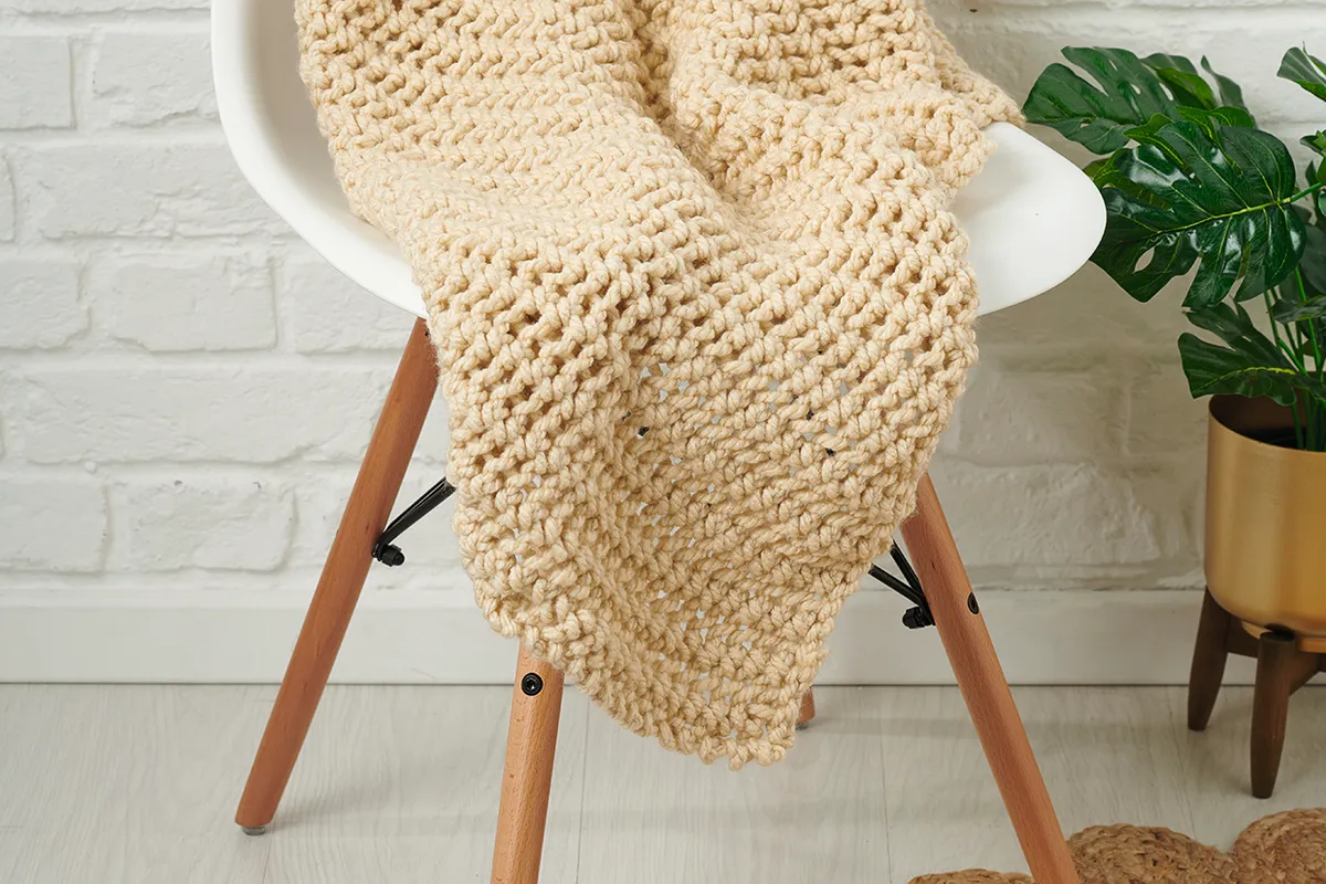 a chunky knit blanket in cream chunky yarn is thrown across a white dining chair