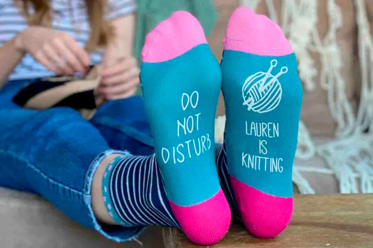 The personalised knitting socks have writing and imagery on both soles, one saying do not disturb and the other saying Lauren is knitting with artwork of a ball of yarn on the needle