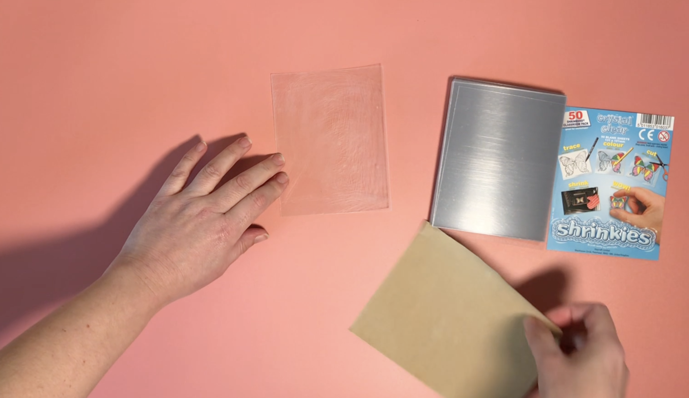 A clear shrink plastic sheet is being rubbed with glass paper to add a surface texture