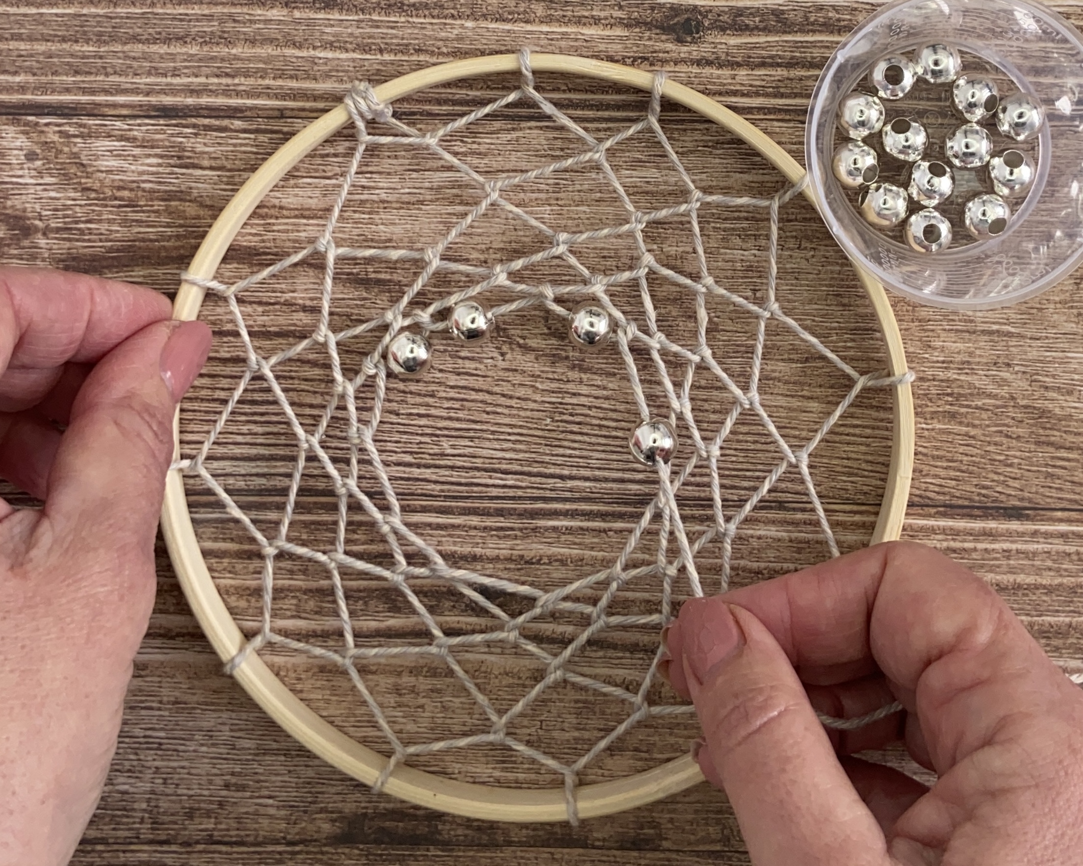 Hand threading bead on to woven loop on dreamcatcher