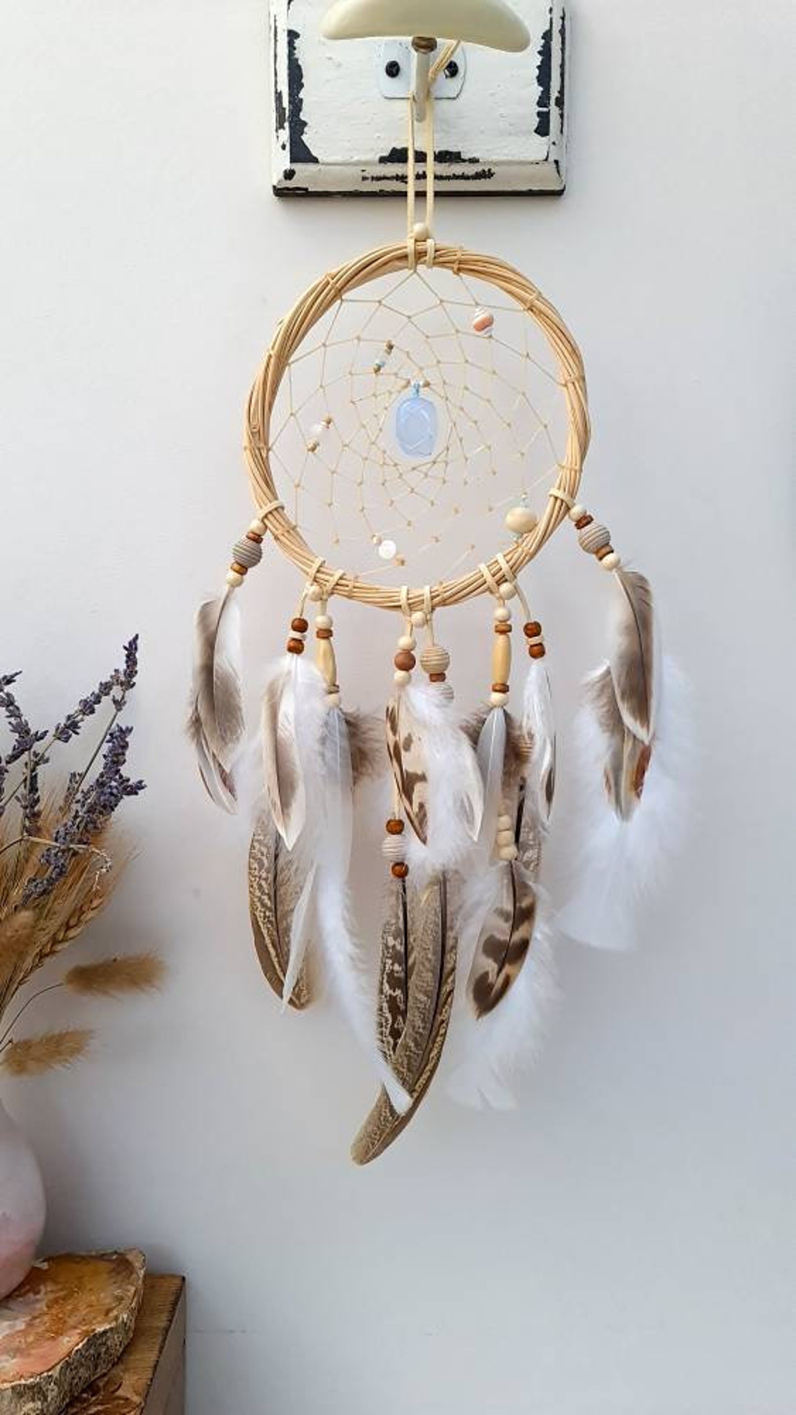 natural feathers and beads hanging from pale dreamcatcher frae with oval blue stone in the centre