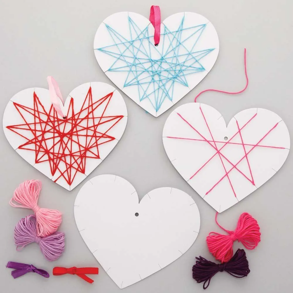 Four paper hearts sit on a table surrounded by string. Each has a different string art design on the front