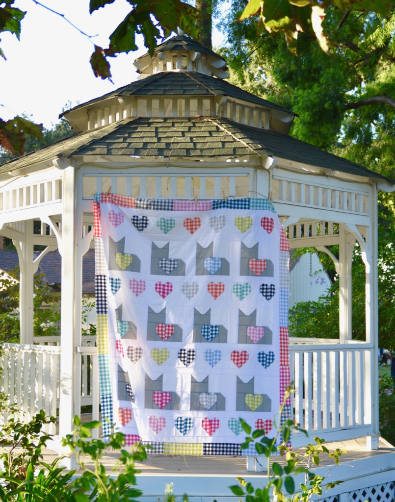 A cats quilting pattern featuring 12 cats shapes is hung from a garden gazebo