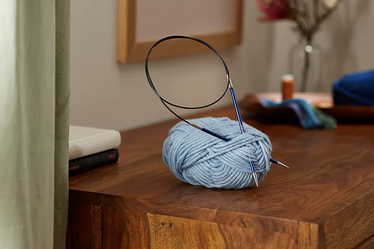 A circular needles is sticking a ball of blue yarn on a dark table