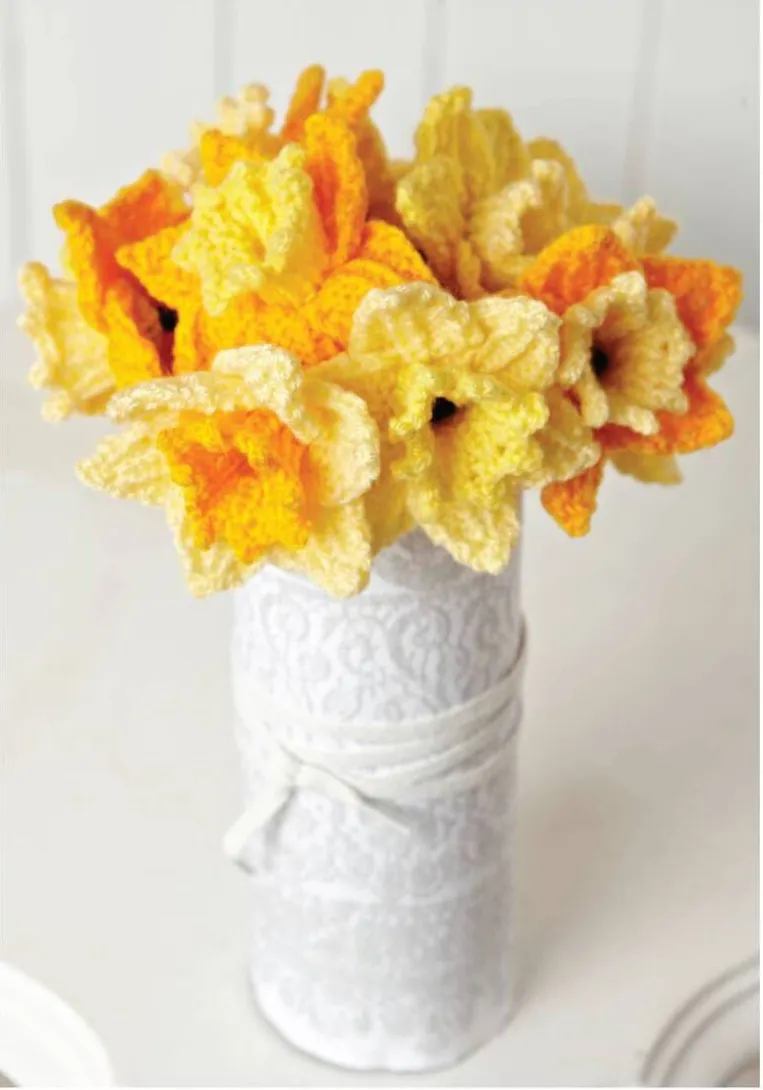 The daffodil free knitted flower pattern has been knitted eight times in different shades of yellow and orange displayed in a white vase