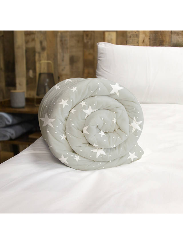 a weighted blanket uk with a white star pattern on a grey fabric background is rolled into a coil on a bed with a lava lamp visible in the background