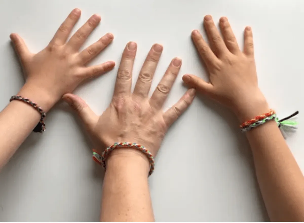 Three hands wearing handmade friendship bracelets