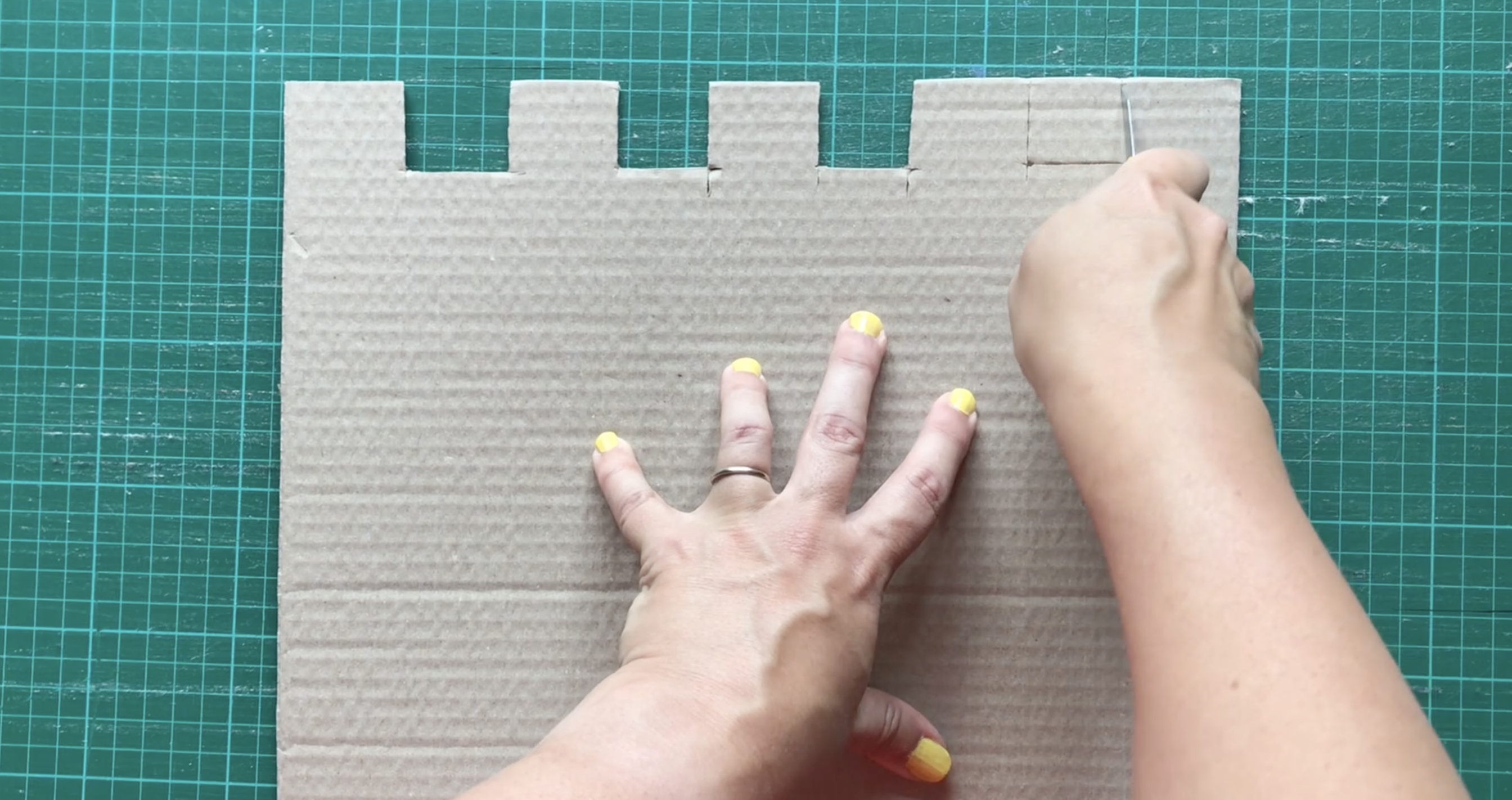 Hands cutting squares from the top of a sheet of cardboard to make castle battlements