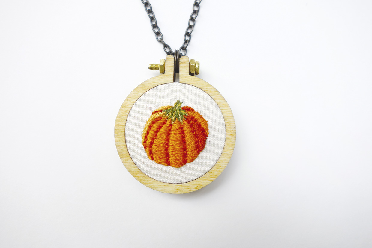 a completed embroidered pumpkin in a necklace