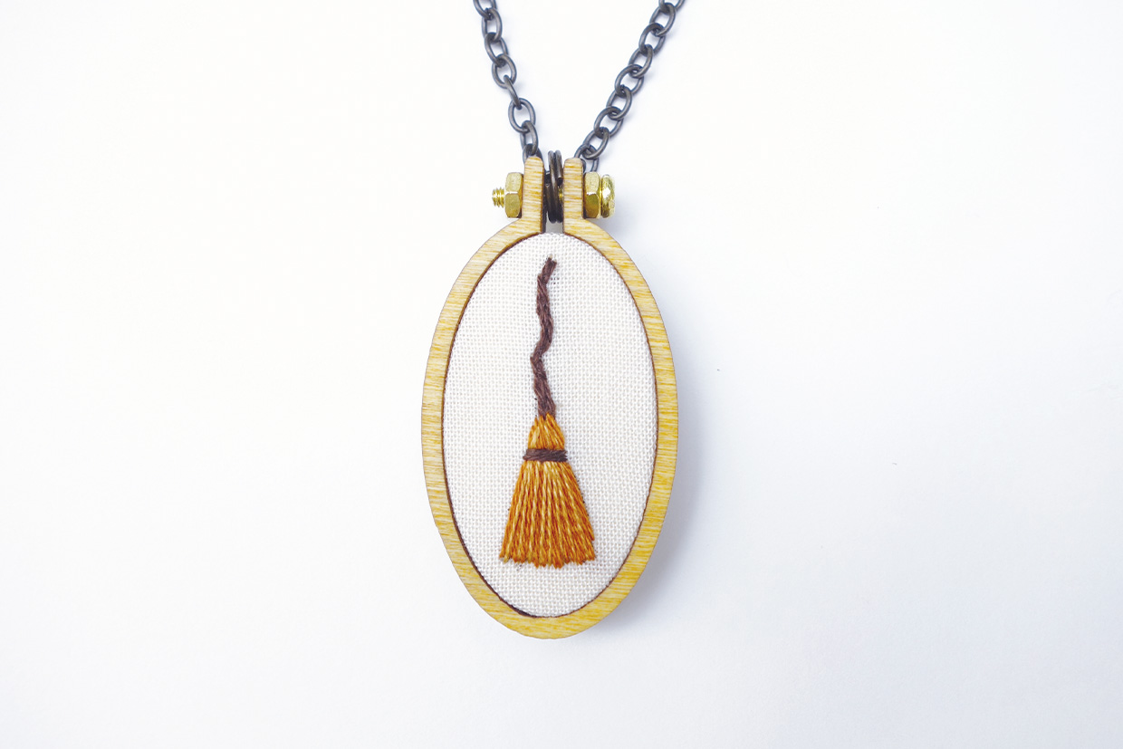 an embroidered broom in a necklace