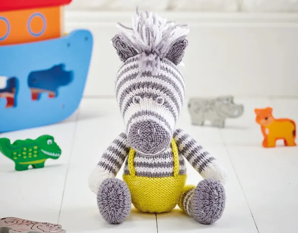 Cute knitted zebra sitting down and wearing yellow dungarees