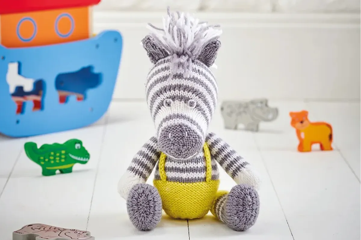 Cute knitted zebra sitting down and wearing yellow dungarees