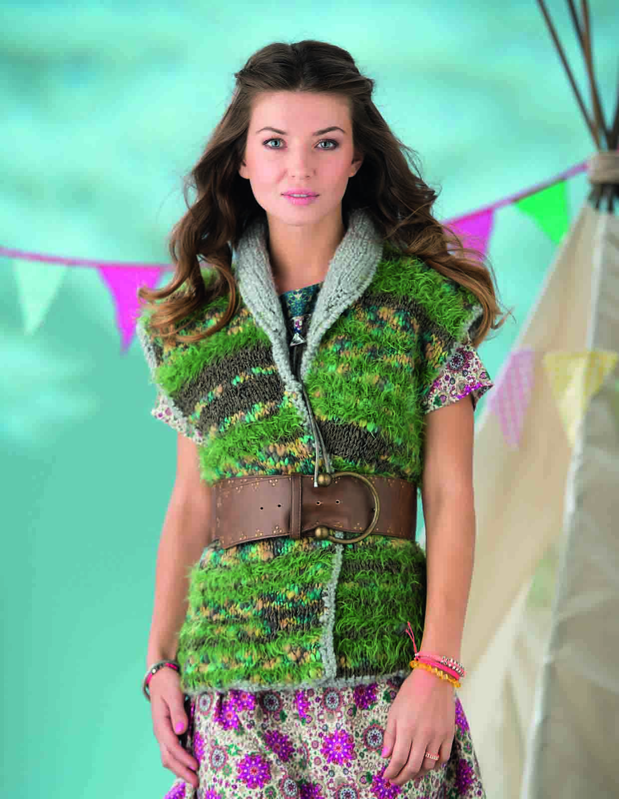 A lady wears a chunky knitted waistcoat in patches of green and brown with a grey knitted collar on show