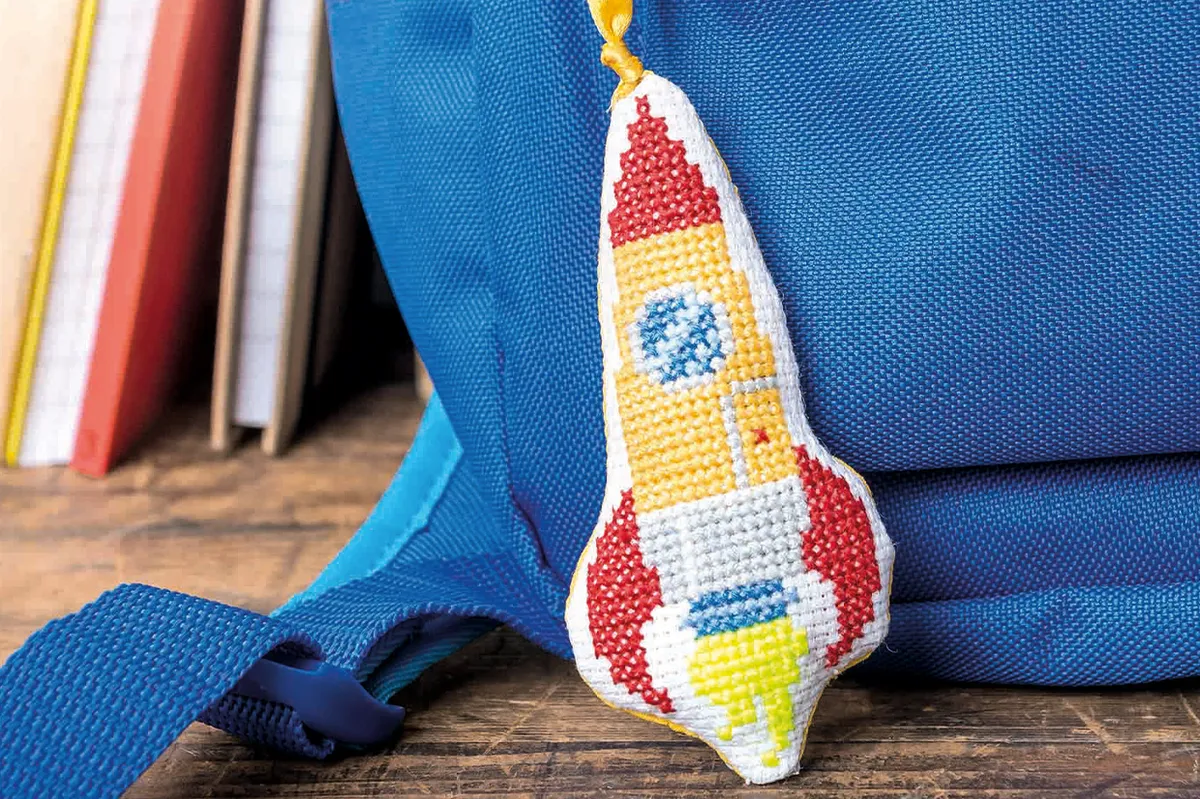 a rocket ship cross stitch attached to a backpack