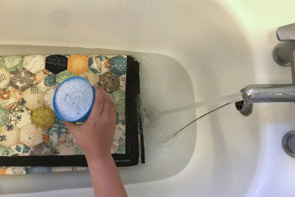 pouring detergent over a quilt to wash it in a bath