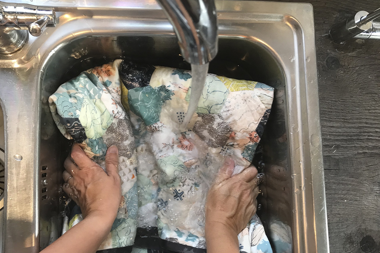 Hands soaking a quilt in a kitchen sink