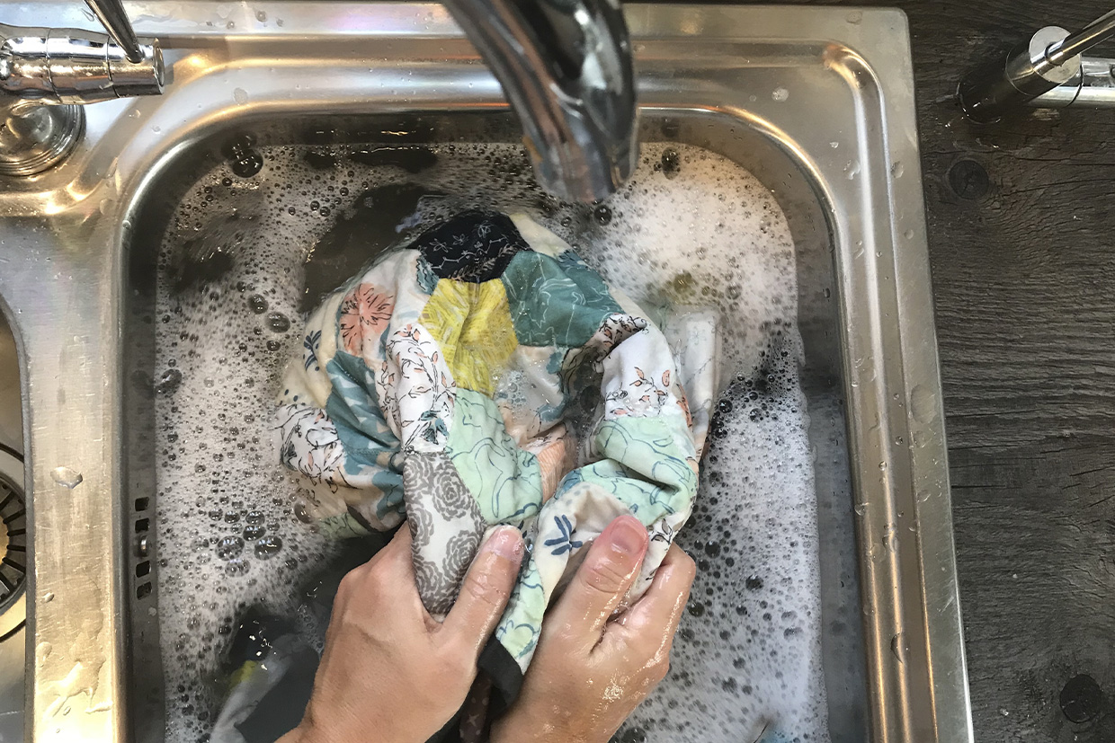 Hands squeezing a quilt in a kitchen sink to wash it