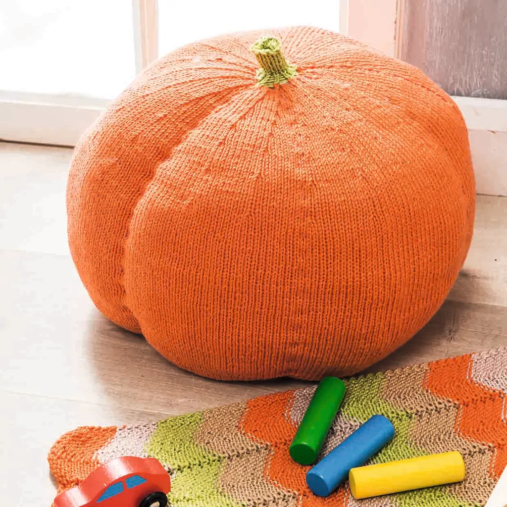 a big swishy orange knitted pumpkin squats on the floor surround by big crayon sticks. Comfy and fun!